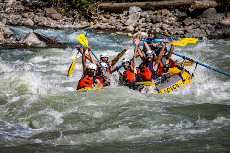 Group of smiling adults splashed by water while whitewater rafting through rapids